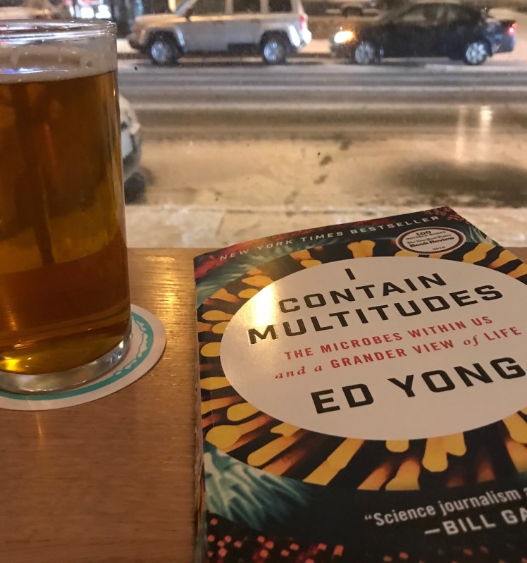 Ed Yong's Book "I Contain Multitudes" on a bar with a pint of beer to the left